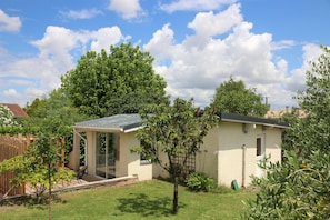 Ein kleines, eingeschossiges Gebäude mit Glasfassade, umgeben von einer gepflegten Rasenfläche und verschiedenen Bäumen.