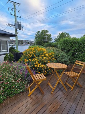 Um deck de madeira com duas cadeiras e uma mesa, cercado por diversas flores e plantas.