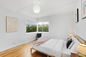 Quarto com cama, uma cadeira, janela com persianas e luminária pendente.