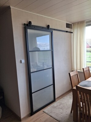 A room with a sliding glass door, a dining table with chairs, and a window with curtains. - Seaside Apartment with Sea Views in Marina Wendtorf (Wendtorf)