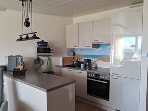 A modern kitchen with white cabinetry, a built-in oven, a microwave, and a coffee maker. - Seaside Apartment with Sea Views in Marina Wendtorf (Wendtorf)