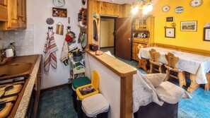 A compact kitchen with a sink, stove, and wooden cabinets. A dining area with a table and chairs is visible. - GRAN PARADIS (San Pietro)