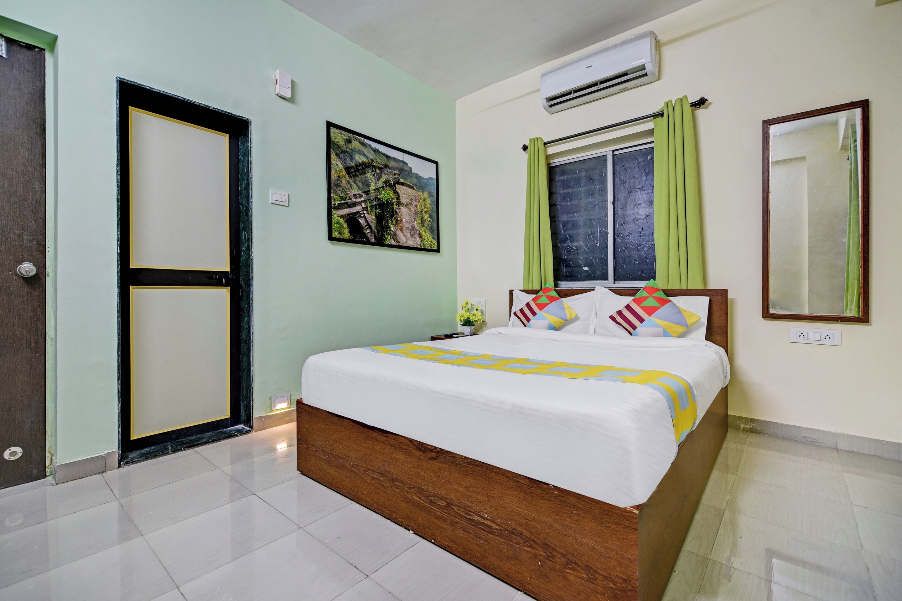 Une chambre d’hôtel avec un lit, une fenêtre avec des rideaux, un appareil de climatisation et une porte.
