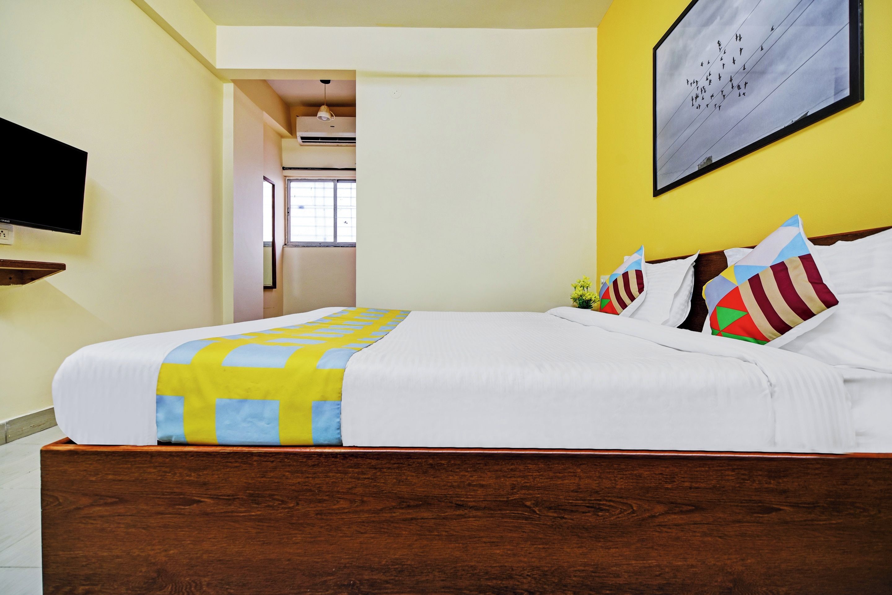 Quarto de hotel com cama, televisão na parede e janela.