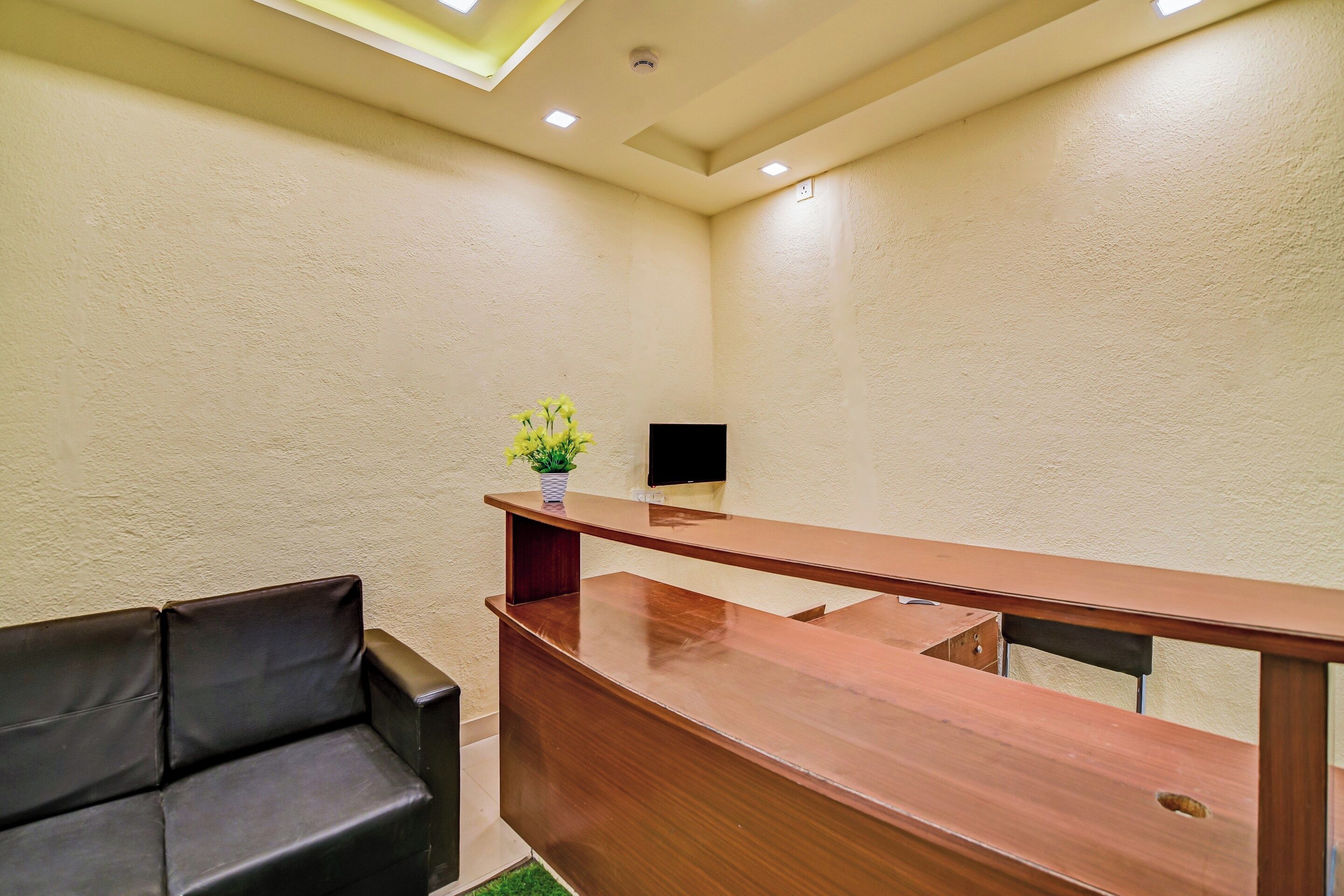 A hotel reception area with a wooden desk, a black leather sofa, and a small vase with yellow flowers.