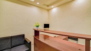 A hotel reception area with a wooden desk, a black leather sofa, and a small vase with yellow flowers.