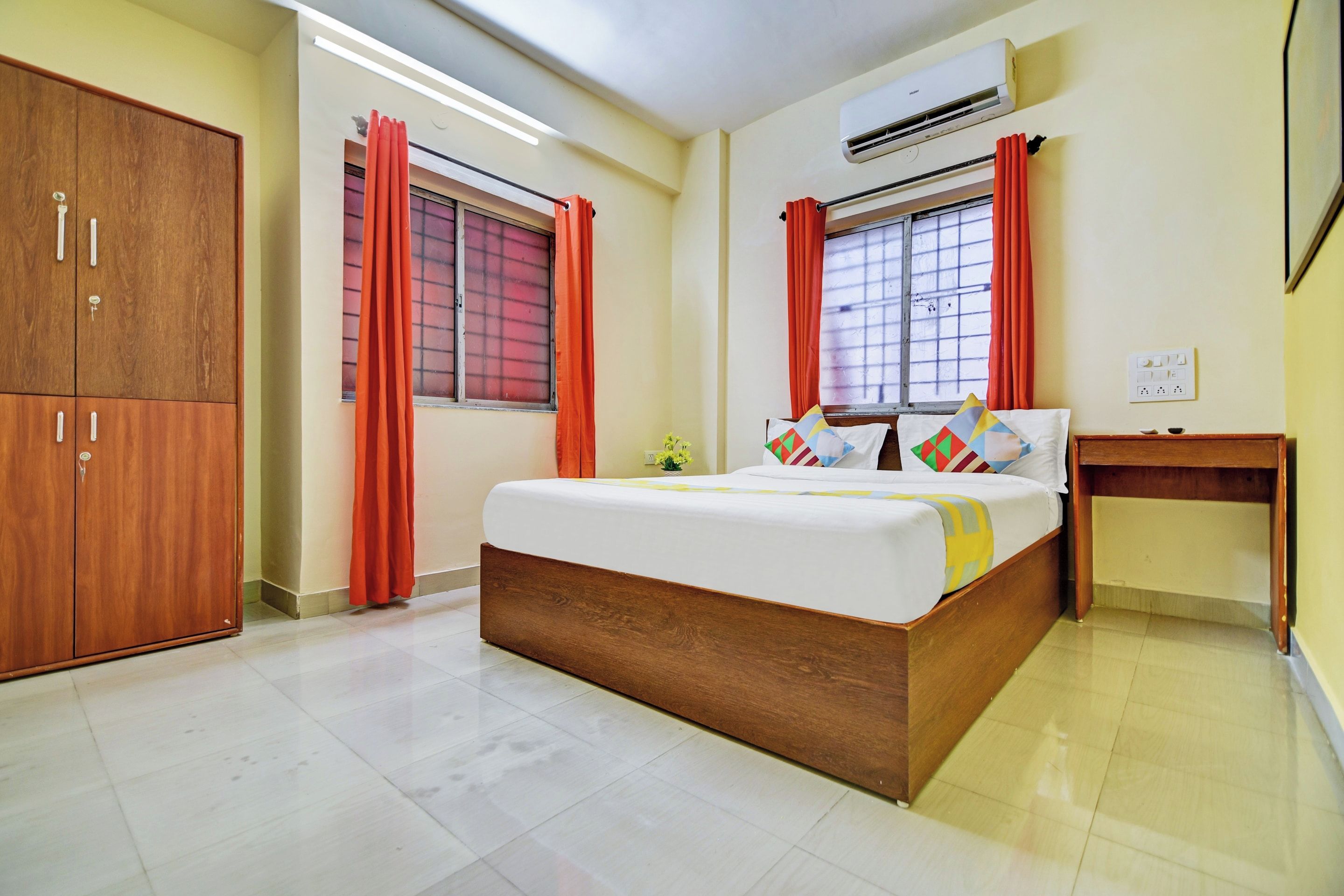 A bedroom with a wooden bed, a wardrobe, an air conditioner, and a window with curtains.