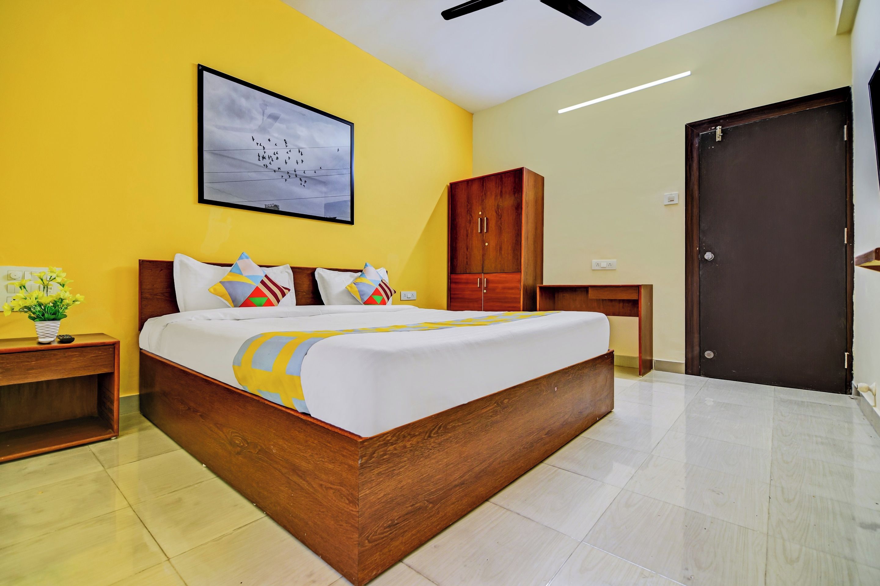 Quarto com cama, mesa de cabeceira, guarda-roupa de madeira, porta e uma obra de arte na parede.