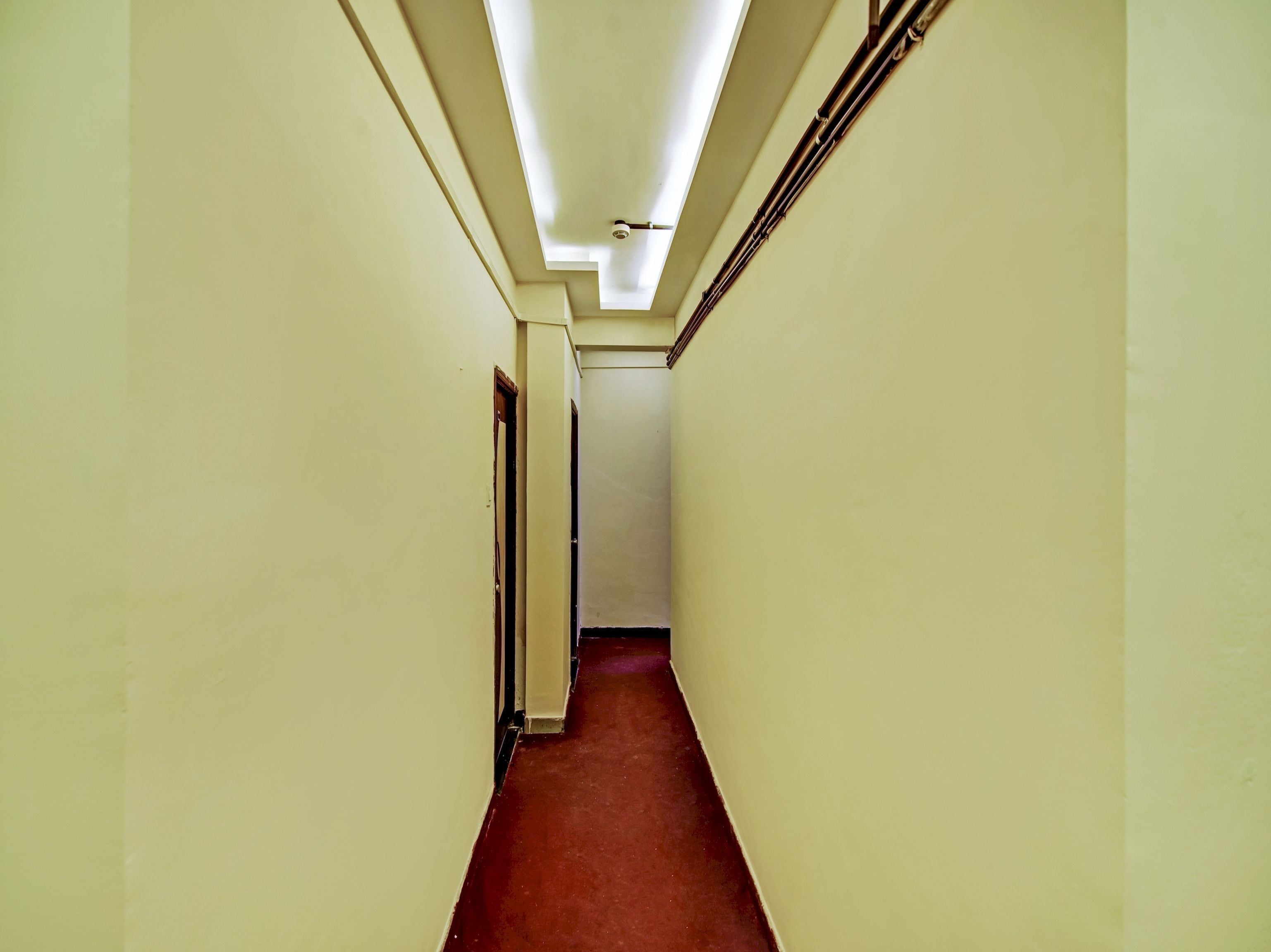 A narrow hallway with a red carpet, white walls, and a ceiling with fluorescent lighting.