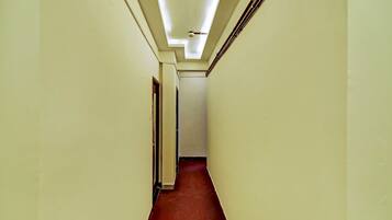 A narrow hallway with a red carpet, white walls, and a ceiling with fluorescent lighting.