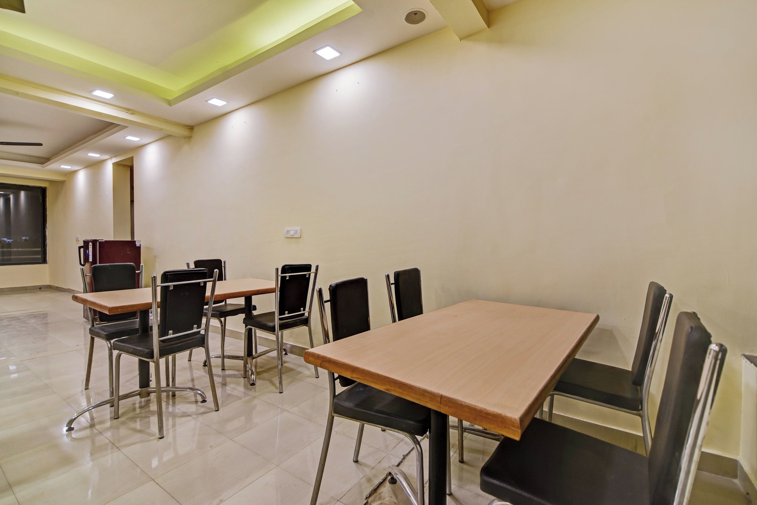 A conference room with tables and chairs, a power outlet on the wall, and a window with blinds.