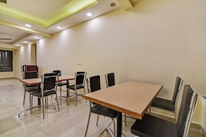 Un salón de conferencias con mesas y sillas, un enchufe en la pared y una ventana con persianas.