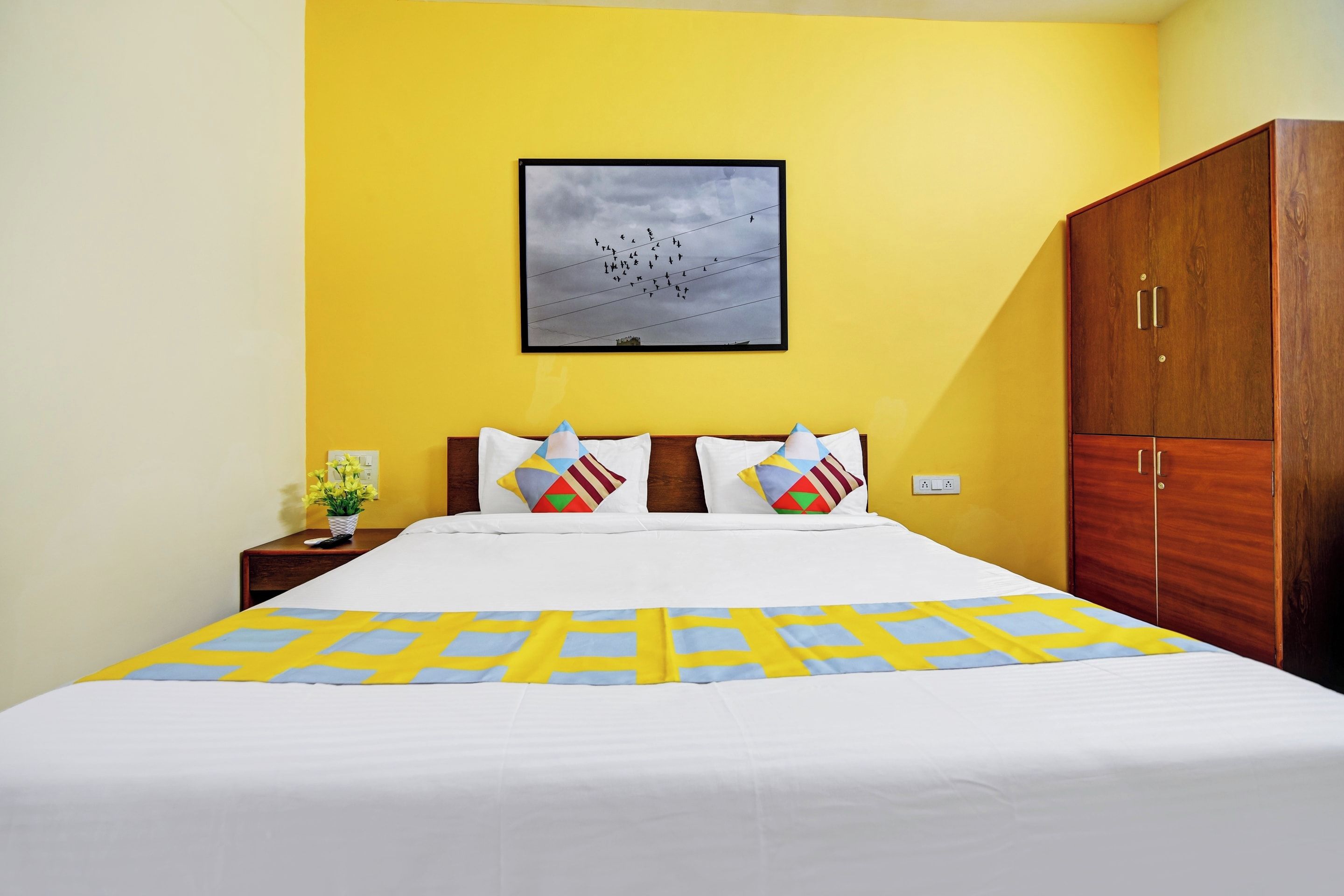 A hotel room with a bed, a nightstand, a wooden wardrobe, and a framed picture on the wall.