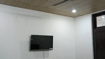 Una habitación con ventilador de techo, televisor montado y una puerta con ventana.