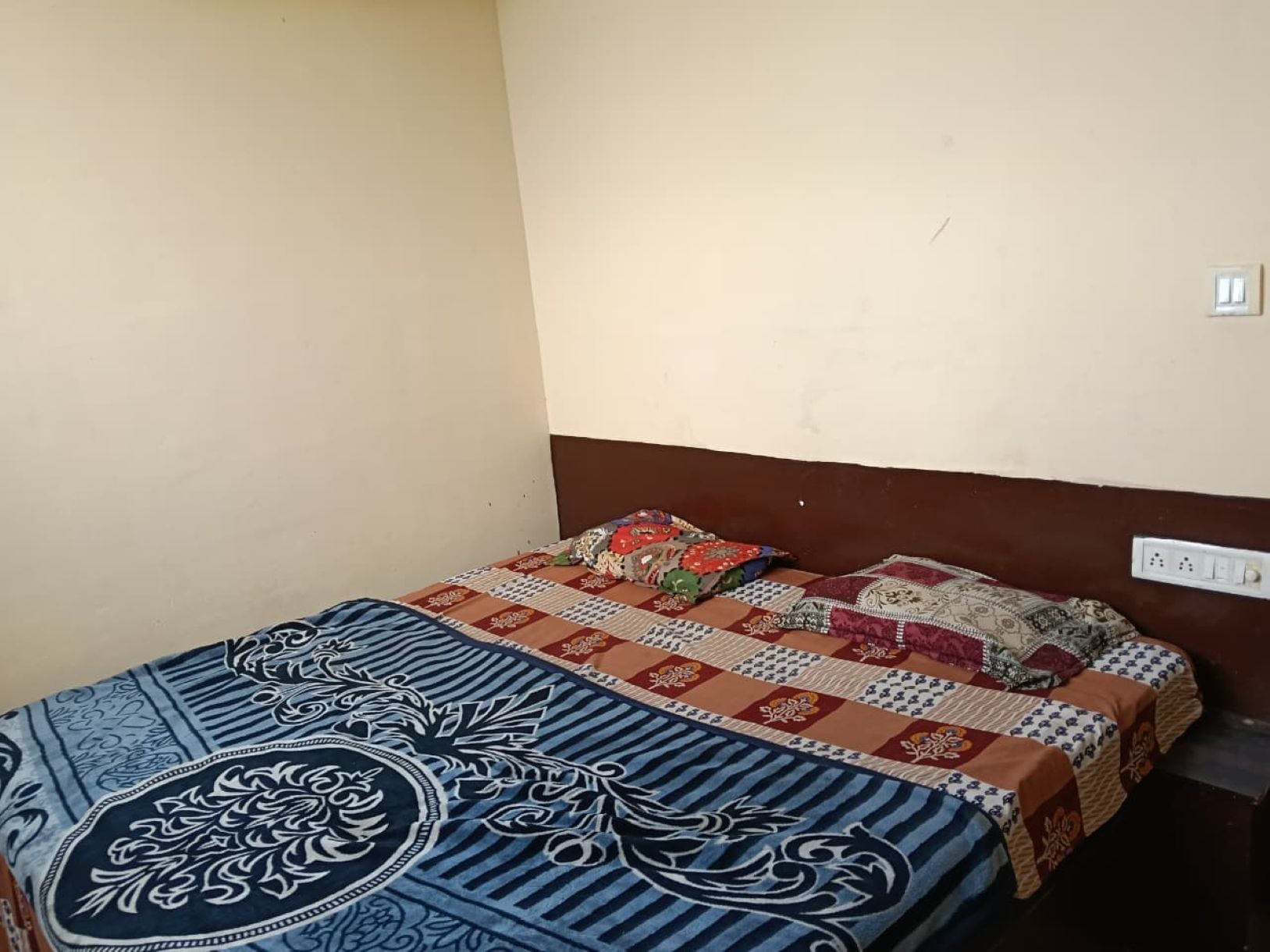 Una cama individual con una colcha estampada y almohadas, un enchufe de pared y una pared lisa.