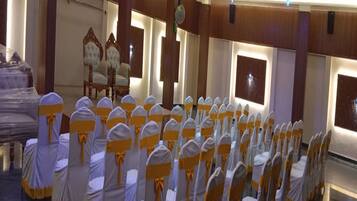 A conference room with rows of chairs covered in white and yellow sashes, wooden paneling on the walls, and a chandelier.