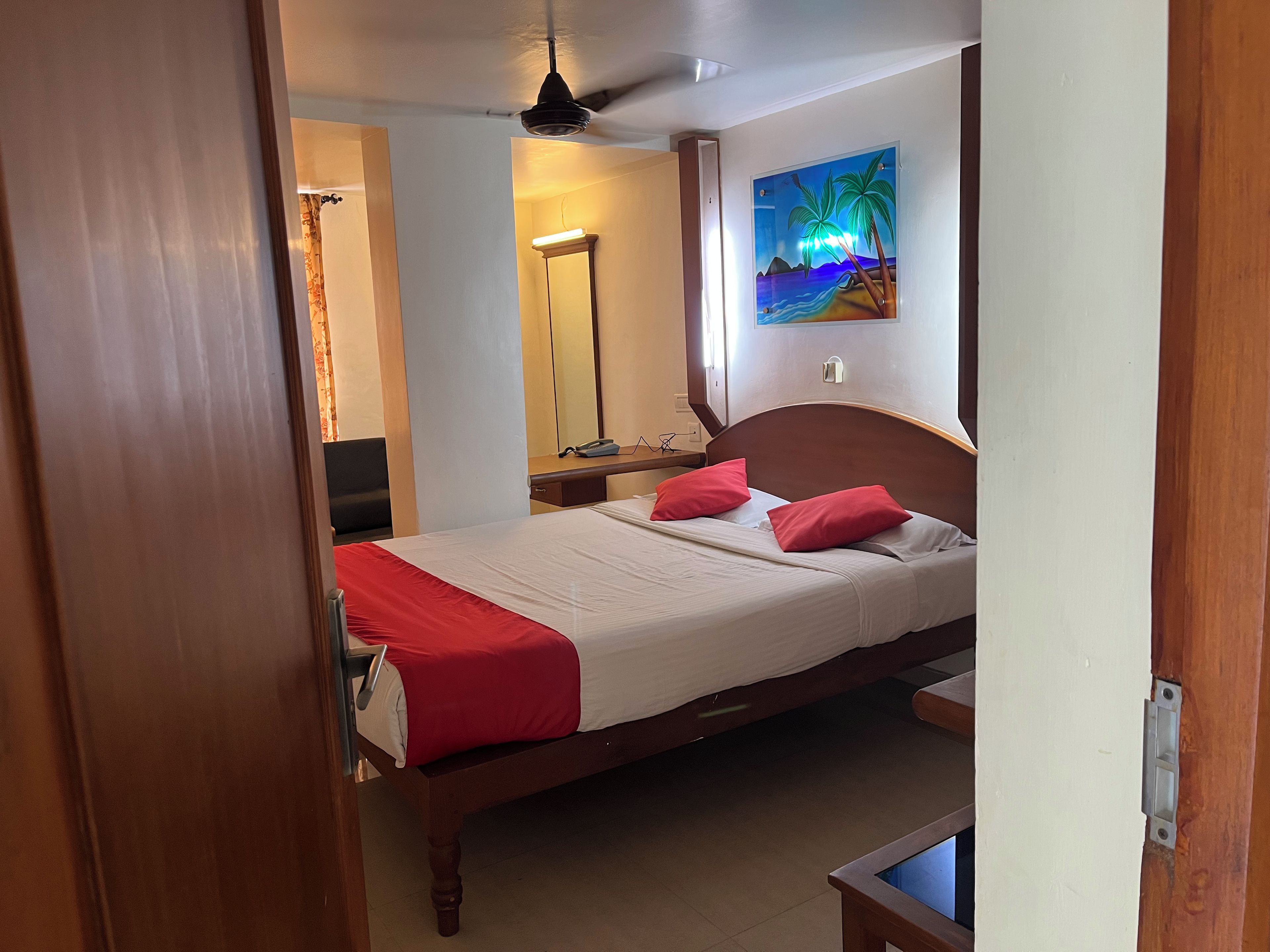 A hotel room with a bed, a desk, a chair, a mirror, and a painting on the wall.