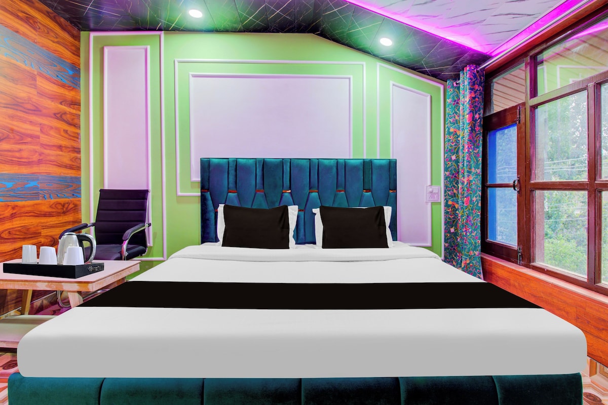 A hotel room with a large bed, a chair, a table with a tray of cups, and a window with curtains.