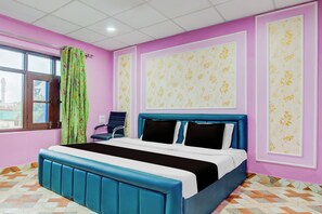 Un dormitorio con cama, una silla, ventana con cortinas y papel tapiz estampado.