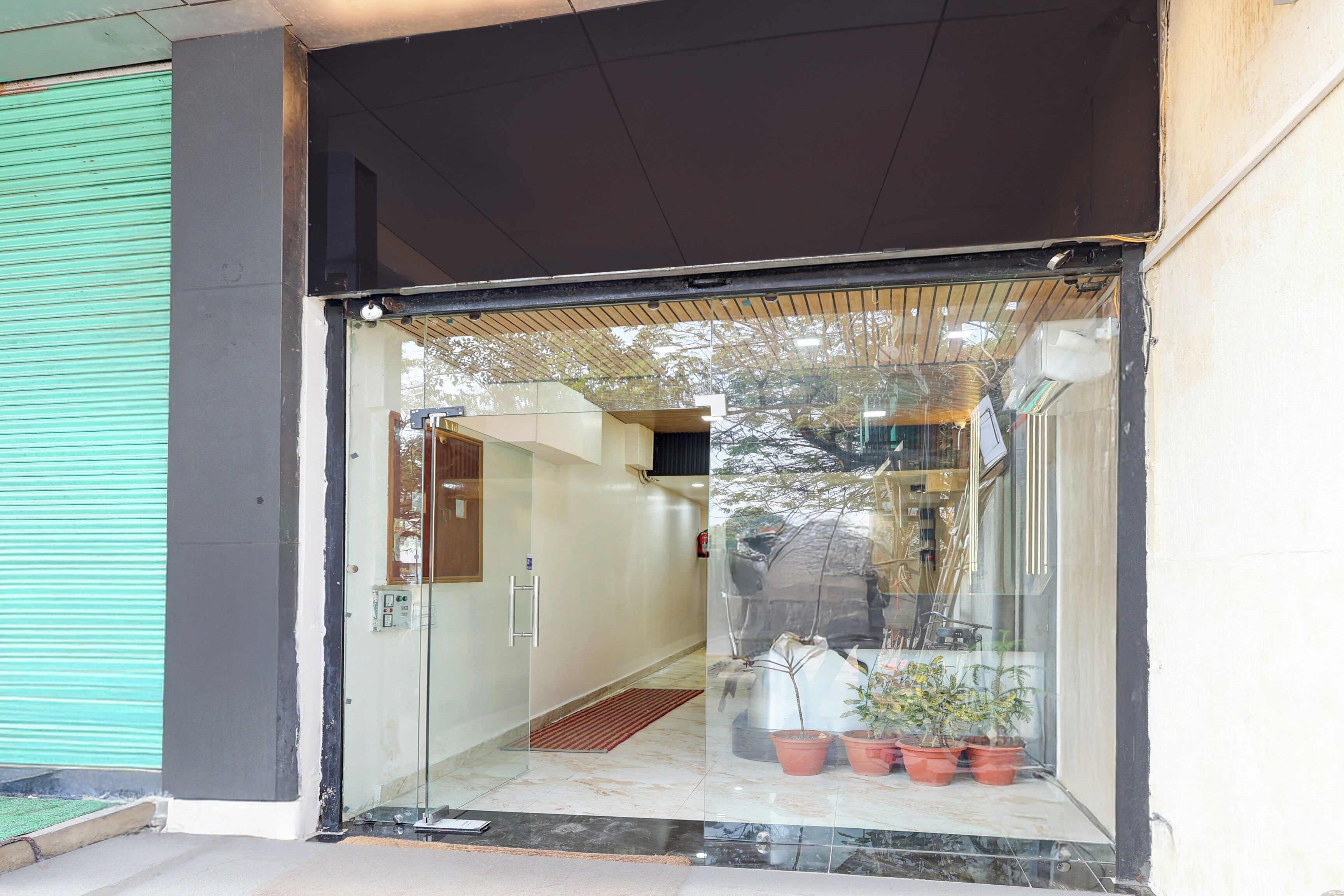 A hotel entrance with a glass door, a reception desk, and potted plants inside.