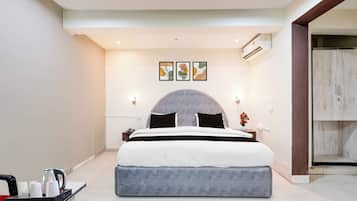 A modern hotel room with a large bed, a bedside table with a kettle, and a small table with cups.