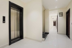 A clean, modern hallway with a polished floor, a closed elevator, and a staircase leading to another level. - Townhouse Indore Airport Formerly (Indore)