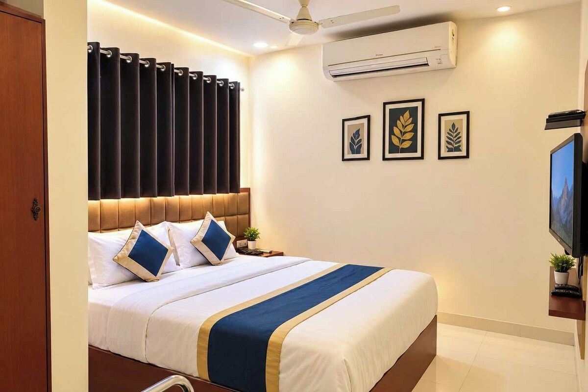 A hotel room with a bed, a TV, an air conditioner, and framed artwork on the wall.