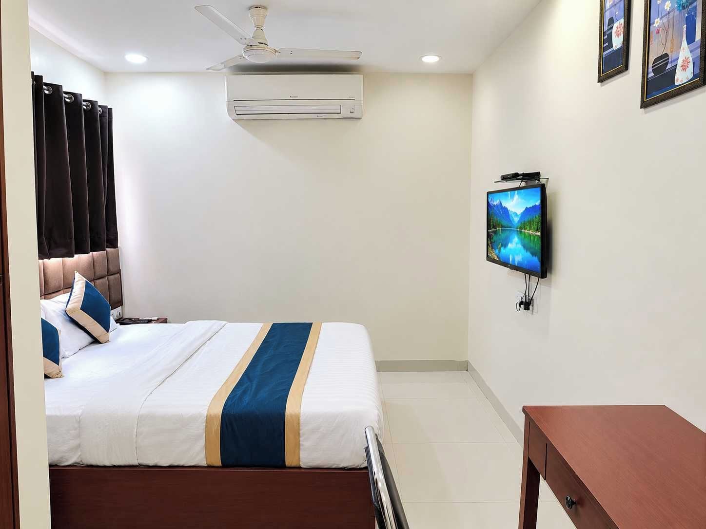 A hotel room with a bed, a television, an air conditioning unit, and a ceiling fan.