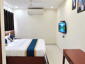 A hotel room with a bed, a television, an air conditioning unit, and a ceiling fan. - Townhouse Indore Airport Formerly (Indore)