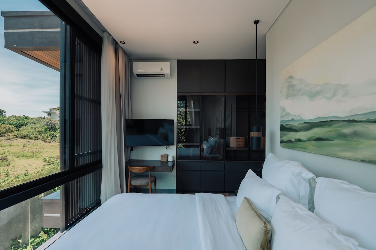 A modern bedroom with a large bed, a desk, and a painting.
