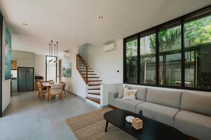 A modern interior with a staircase, a sofa, a dining area, and large windows. - Bellana Villas (Jimbaran)