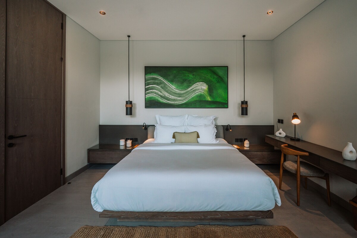 A modern bedroom with a large bed, two bedside tables, a nightstand, and a wall-mounted abstract painting.
