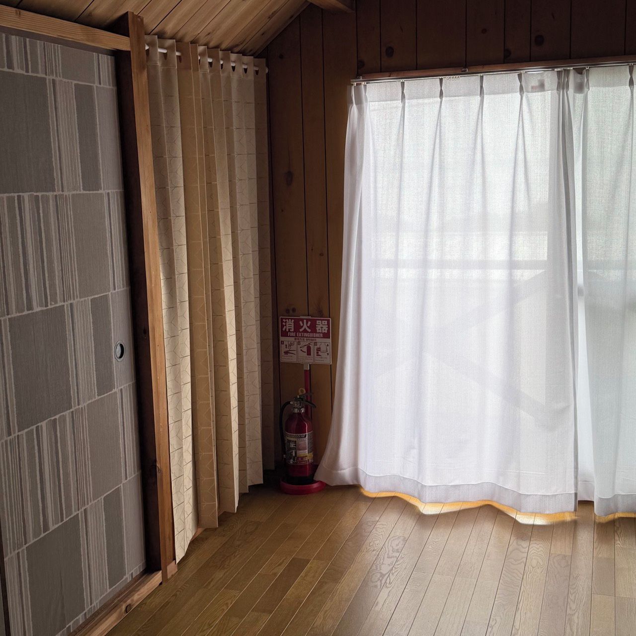 Ein Zimmer mit Holzboden, einer Schiebetür, einem Feuerlöscher und einem Vorhang.