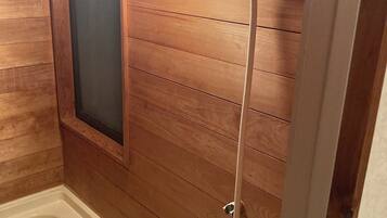 Une salle de bain aux murs lambrissés, équipée d’une baignoire, d’une pomme de douche et d’un luminaire fixé au mur.