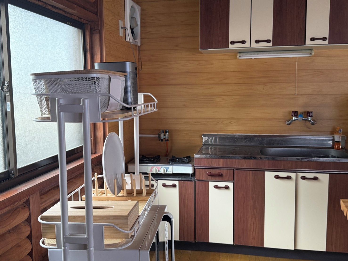 Une cuisine de taille réduite, avec des meubles de rangement en bois, un évier, une cuisinière et une petite fenêtre.