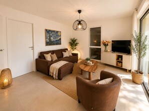 A modern living room with a sofa, armchair, and a TV on a stand. - Apartment with a pool, 8 minutes from downtown (Saint-Rémy-de-Provence)