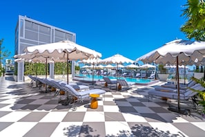 A rooftop pool area with multiple sun loungers and umbrellas, a checkered floor, and a view of the city skyline. - Nomad Vertigo & Amenities (Miami)