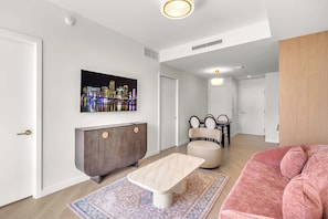 A modern living room with a cityscape painting, a dark wood cabinet, a beige sofa, and a light-colored coffee table. - Nomad Vertigo & Amenities (Miami)