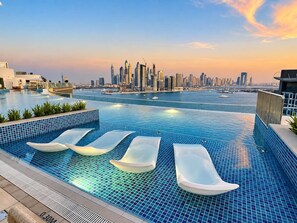 A rooftop infinity pool with lounge chairs and a city skyline view. - Chic Seven Palm Studio | Beach & Rooftop Pool (Dubai)