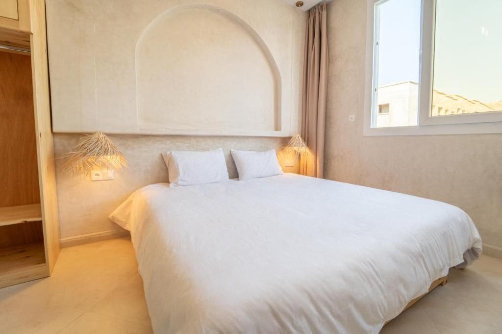 Un dormitorio con cama, lámparas de noche, armario y ventana.