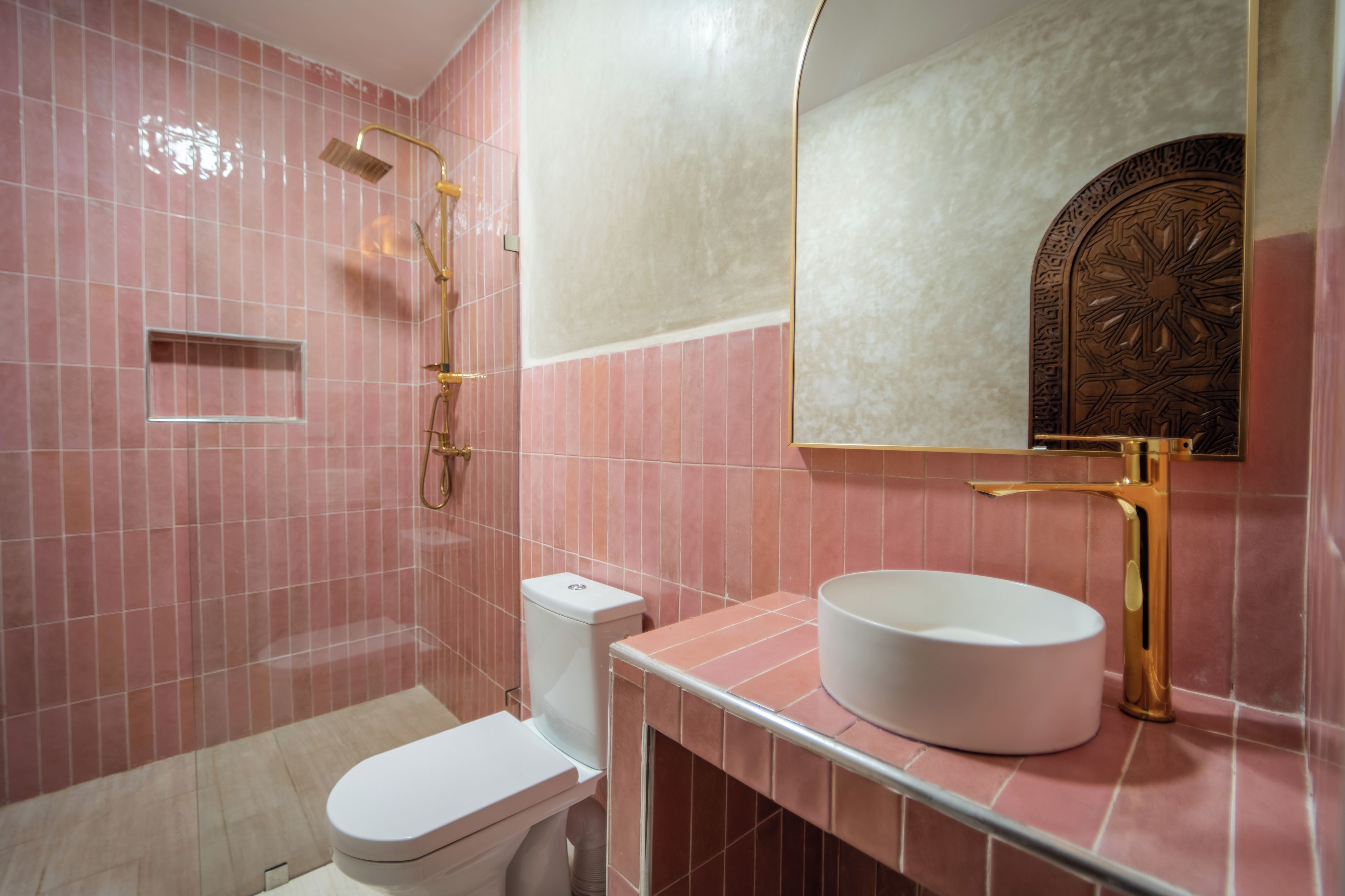 A bathroom with pink tiles, a white toilet, a gold-finished sink, and a mirror with a decorative frame.