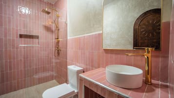 A bathroom with pink tiles, a white toilet, a gold-finished sink, and a mirror with a decorative frame.