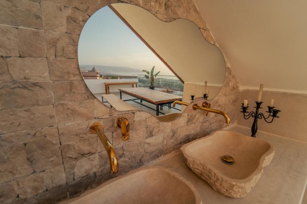 Un baño con un lavamanos de piedra, un espejo que refleja un balcón y una araña.