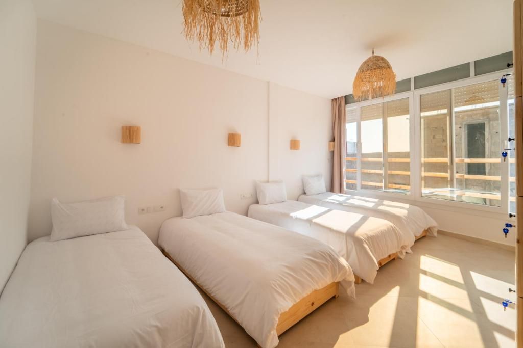 Habitación de hotel con tres camas, un ventanal grande y una lámpara colgante.