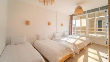 Habitación de hotel con tres camas, un ventanal grande y una lámpara colgante.