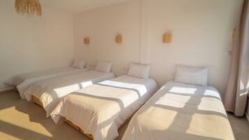 Ein Zimmer mit drei Einzelbetten an einer Wand, jeweils mit Holz Kopfteil und weißer Bettwäsche.