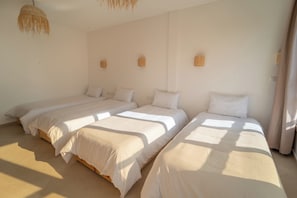 A room with three single beds aligned against a wall, each with a wooden headboard and white bedding. - Nomaya Surf House Tamraght (Aourir)