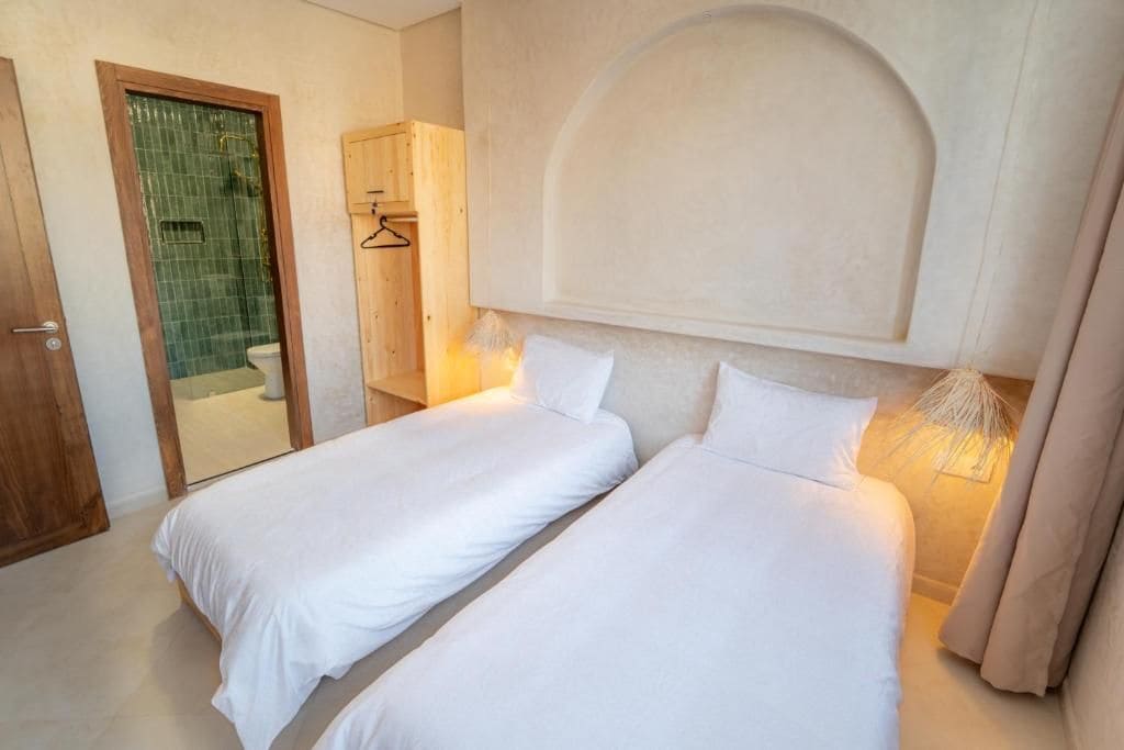Un dormitorio con dos camas, una puerta de madera, una ducha y un perchero para toallas.