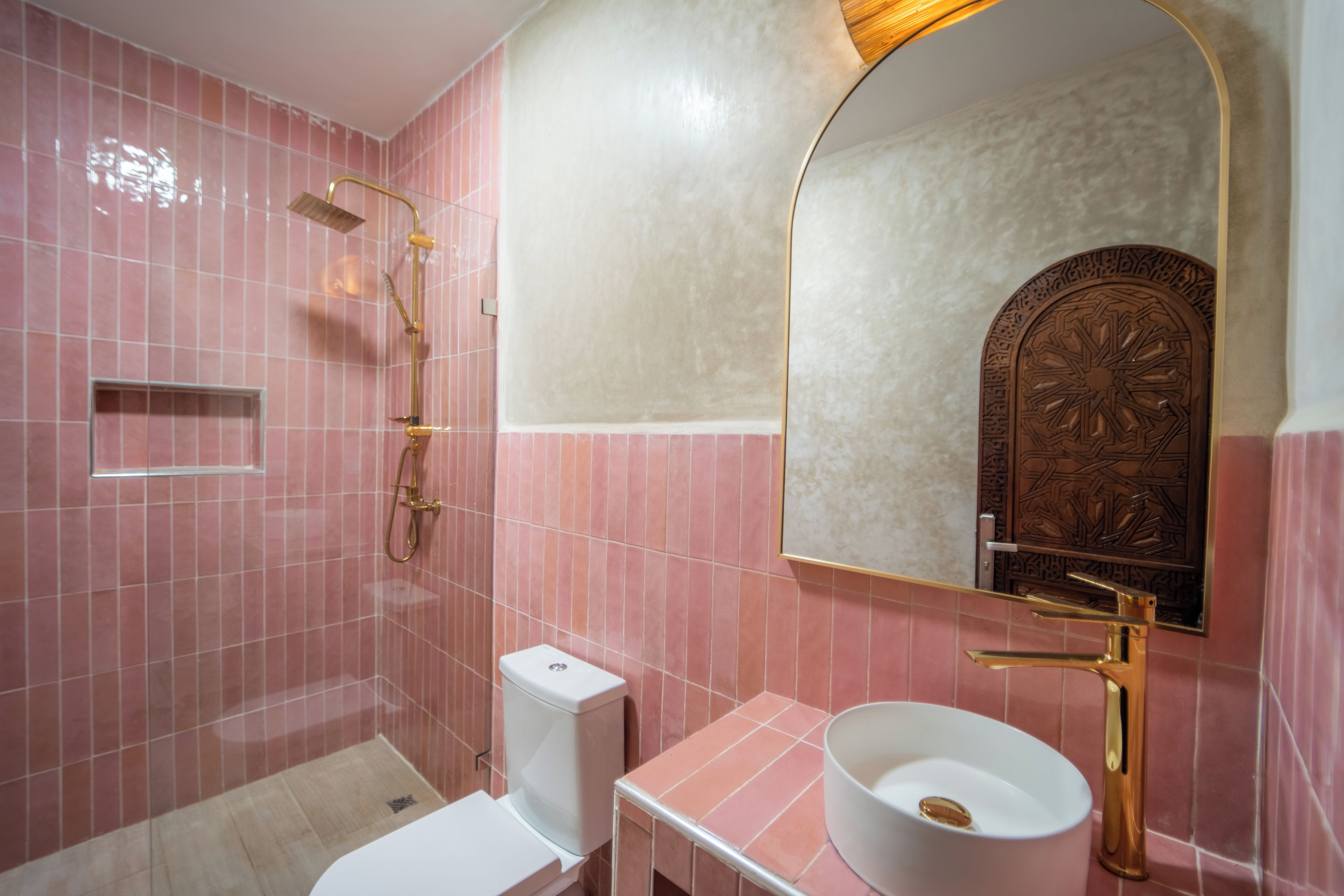 A bathroom with pink tiles, a white sink, a gold faucet, and a shower with a gold showerhead.