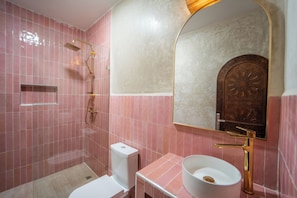 A bathroom with pink tiles, a white sink, a gold faucet, and a shower with a gold showerhead. - Nomaya Surf House Tamraght (Aourir)